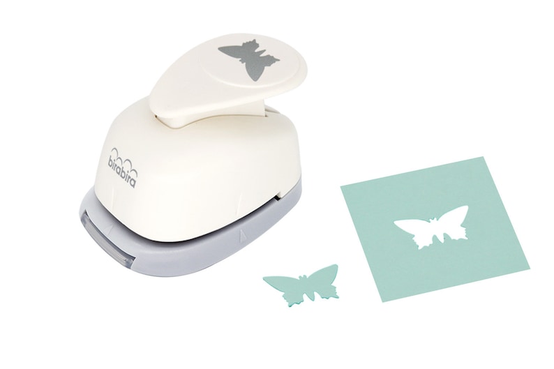 May include: A white paper punch with a gray butterfly design on the top. The punch is used to create butterfly shapes from paper. A green butterfly shape has been punched out of a piece of green paper.