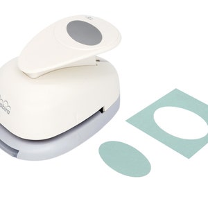 May include: A white oval punch with a gray handle and a gray button. The punch is used to create oval shapes in paper. Two oval shapes are shown, one on a light blue square and one on a white background.