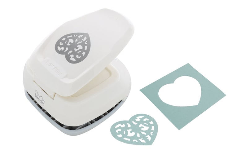 May include: White paper punch with a heart-shaped design. The punch is open and shows the heart-shaped cut-out. A sample of the cut-out is shown in light blue paper.