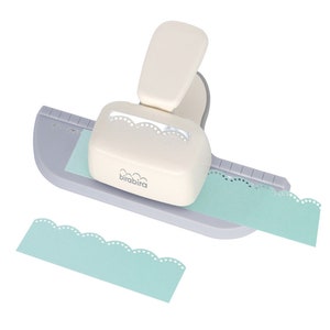 May include: A white and gray paper punch with a blue guide and a light blue piece of paper with a scalloped edge. The punch is labeled "brabibra".