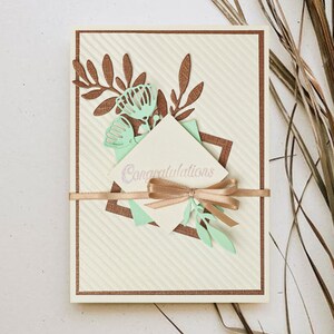 May include: A white card with a brown border and a green and brown floral design. The card has a white envelope with the word "Congratulations" written on it.