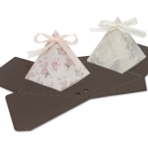 May include: Two pyramid-shaped gift boxes with floral and patterned designs. The boxes are made of paper and have a brown cardboard base. The boxes are tied with ribbons and are ready for gift giving.