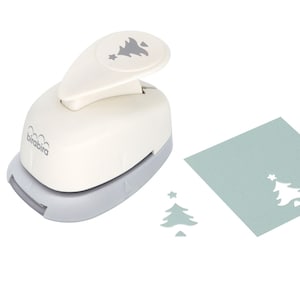 May include: White and gray paper punch with a Christmas tree design. The punch is on a white background with a green piece of paper with a punched out Christmas tree.