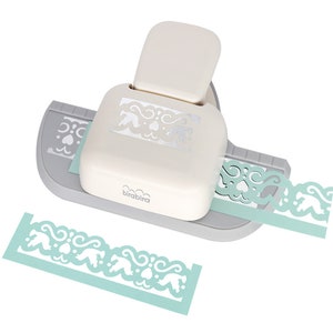 May include: A white and grey paper punch with a decorative border design. The punch is creating a light blue paper border with a repeating pattern of hearts and swirls. The punch is labelled "birabibra".
