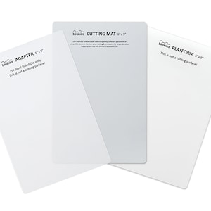 May include: Three white cutting mats for a craft machine. The mats are labeled "Adapter 6"x9"", "Cutting Mat 6"x9"", and "Platform 6"x9"". The text on the mats indicates that the adapter is for steel ruled die only and is not a cutting surface. The cutting mat is a cutting surface. The platform is not a cutting surface.