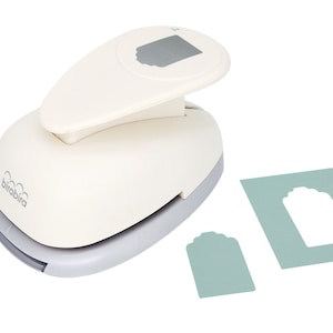 May include: White paper punch with a gray handle, used to create tag shapes. The punch is shown next to a sample tag and a sheet of paper with a tag-shaped hole.