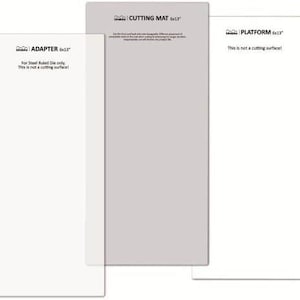 Könnte beinhalten: Drei weiße rechteckige Schneidematten, jede mit einem anderen Etikett. Die erste Matte ist mit "ADAPTER 6x13" beschriftet und trägt den Hinweis "Nur für Stahl-Lineal-Matrizen. Dies ist keine Schneidefläche!" Die zweite Matte ist mit "CUTTING MAT 6x13" beschriftet. Die dritte Matte ist mit "PLATFORM 6x13" beschriftet und trägt den Hinweis "Dies ist keine Schneidefläche!"