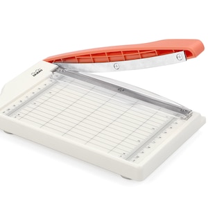 May include: A white paper trimmer with a clear cutting guide and an orange handle. The trimmer has a ruler on the side and a grid pattern on the cutting surface.