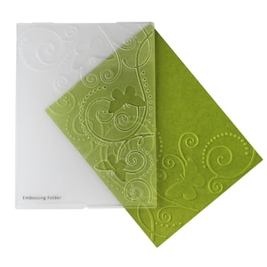 May include: A clear plastic embossing folder with a green embossed design of swirling vines and butterflies. The text "Embossing Folder" is printed on the folder.