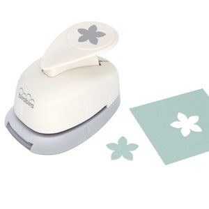 May include: White paper punch with a gray base. The punch is shaped like a flower and has a gray handle. The punch is shown with a white flower punched out of a light blue piece of paper.