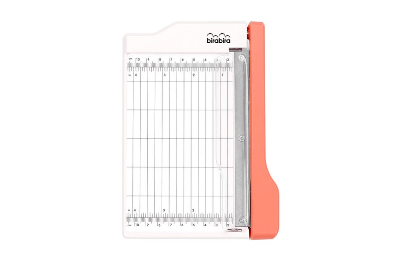 May include: A white paper trimmer with a red handle and a metal blade. The trimmer has a grid pattern and measurements in inches.