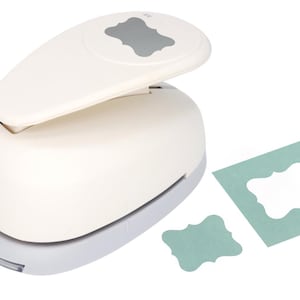 May include: A white label punch with a gray base and handle, alongside a teal paper cutout and a punched-out label. The punch has a gray label-shaped design on top. The brand name "bitabira" is printed on the side.