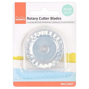 May include: A pack of Bira Craft rotary cutter blades. The package is white, orange, and blue. The blades are silver and have a scalloped edge. The package text reads "Rotary Cutter Blades" and "Cuchillas de Corte Rotatorias | Lames de Coupe Rotatives".