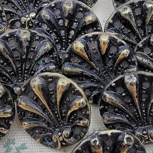 May include: A group of 10 black and gold metal buttons with a decorative fan-shaped design. The buttons are round and have a raised design.
