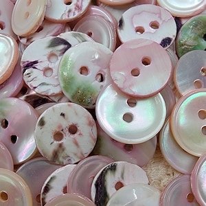 May include: A selection of iridescent buttons in shades of pink, white, and green. The buttons are round with two or four holes. Some have a marbled effect. Ideal for sewing projects.