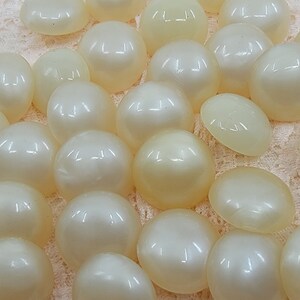 May include: A collection of 25 off-white round buttons with a glossy finish.