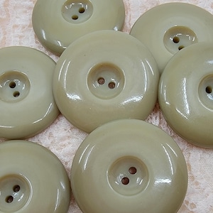 May include: Six beige plastic buttons with two holes each. The buttons are round and have a smooth, glossy finish.