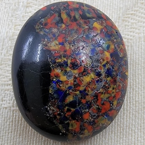 May include: A round, black glass button with a colourful, speckled pattern. The pattern includes red, yellow, blue, and gold flecks.