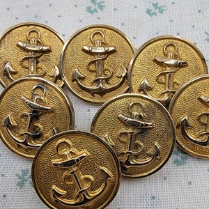 May include: Eight gold-colored metal buttons with an anchor design. The anchors are detailed with a rope-like design and are set against a textured background.