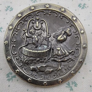 May include: A round, antique-style button with a detailed relief design. The button features a well with a figure and a girl, surrounded by decorative flourishes and small star accents. The color is a muted bronze.