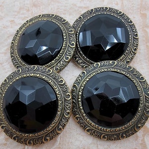 May include: Four black and gold buttons with a faceted glass center. The buttons have a decorative, ornate gold frame.