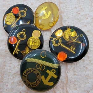 Op de afbeelding: Vijf ronde, kleurrijke hars cabochons met verschillende ontwerpen. De cabochons bevatten gouden sleutels, ankers, sterren en munten. De cabochons zijn perfect voor het maken van sieraden of knutselen.