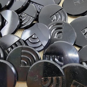 May include: A collection of glossy black buttons. Each button is round with a quarter section carved with concentric arcs. The remaining section is smooth and reflective. The buttons are scattered, showing their design.