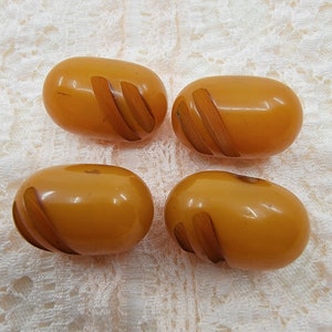 Puede incluir: Cuatro botones de color ámbar con un diseño de espiral. Los botones son de forma ovalada y tienen un acabado brillante.