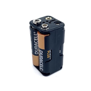 Puede incluir: Un soporte de baterías negro con dos baterías AA Duracell Plus insertadas. El soporte tiene un pequeño interruptor en el lateral.