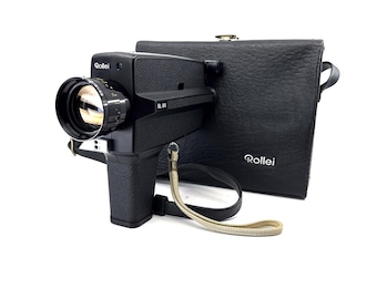Może przedstawiać: Czarna kamera filmowa Super 8 Rollei SL 65 z skórzanym futerałem. Kamera ma czarny pasek i srebrny obiektyw.