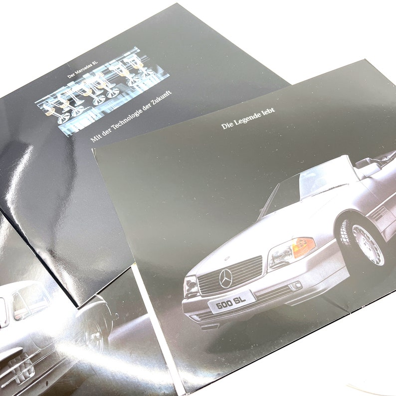 May include: A black and white brochure with a silver Mercedes-Benz 500 SL convertible on the front. The text on the brochure reads "Die Legende lebt" and "500 SL".