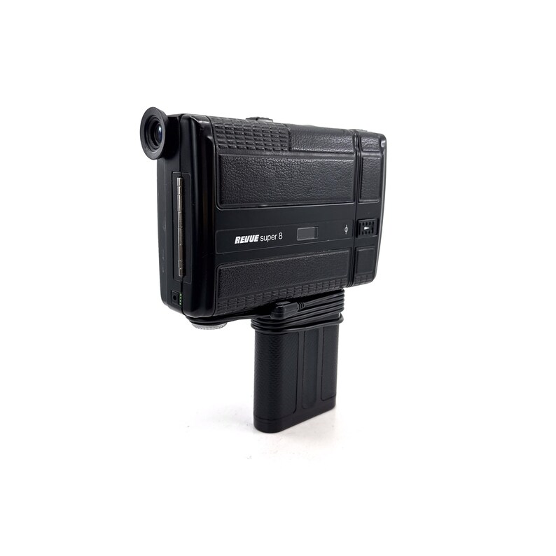 May include: A black Revue Super 8 film camera with a textured body and a lens on the front. The camera is mounted on a black stand.