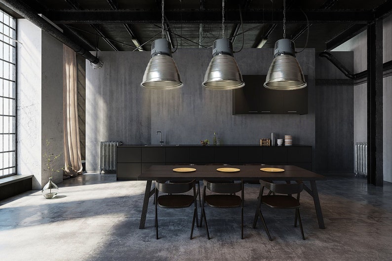 Puede incluir: Comedor de estilo industrial con una mesa de madera oscura y sillas negras. Tres l&aacute;mparas colgantes plateadas cuelgan sobre la mesa. La habitaci&oacute;n tiene suelo y paredes de hormig&oacute;n, con una gran ventana y un mueble negro.