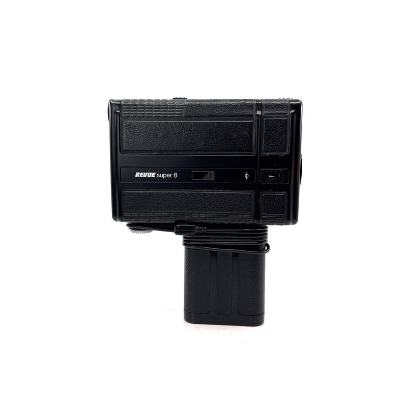 May include: A black Revue Super 8 film camera with a built-in battery pack. The camera has a textured black finish and a silver label with the text "REVUE Super 8".