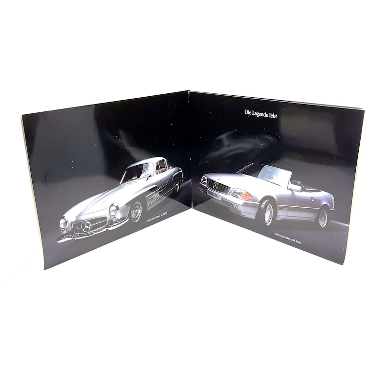 May include: A black and white image of two Mercedes-Benz cars. The car on the left is a silver 1950s model, and the car on the right is a silver 1990s model. The text "Die Legende lebt" is visible on the right side of the image.