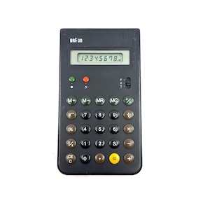 Puede incluir: Una calculadora Braun negra con una pantalla digital que muestra el número 12345678. La calculadora tiene una serie de botones redondos con números y símbolos matemáticos. La marca "BRAUN" está impresa en la parte superior.