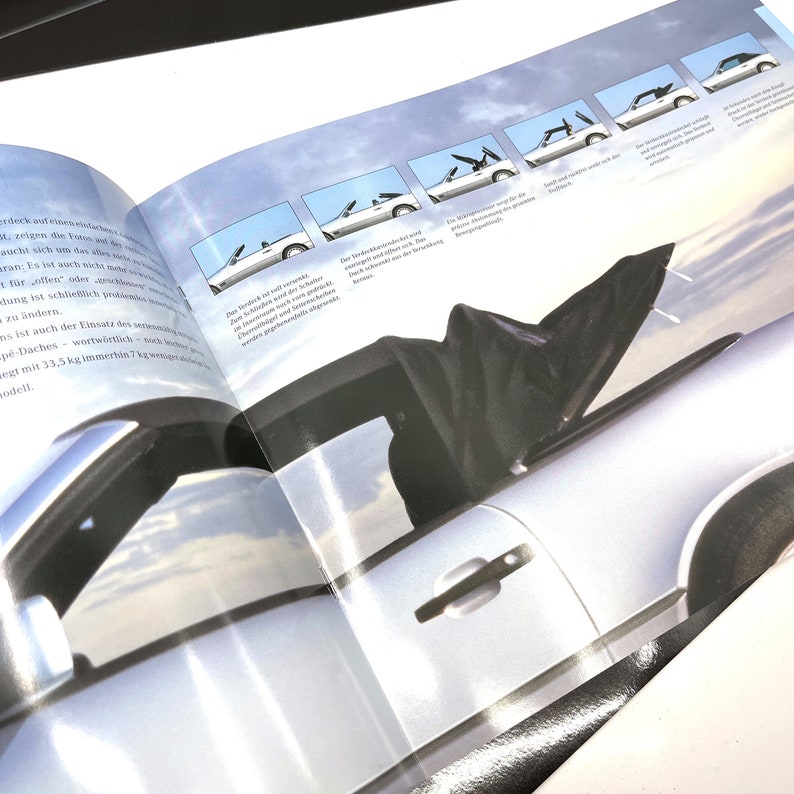May include: A close-up of a silver car with a black fabric roof. The roof is open and the car is parked on a sunny day. The image shows the different stages of the roof opening.