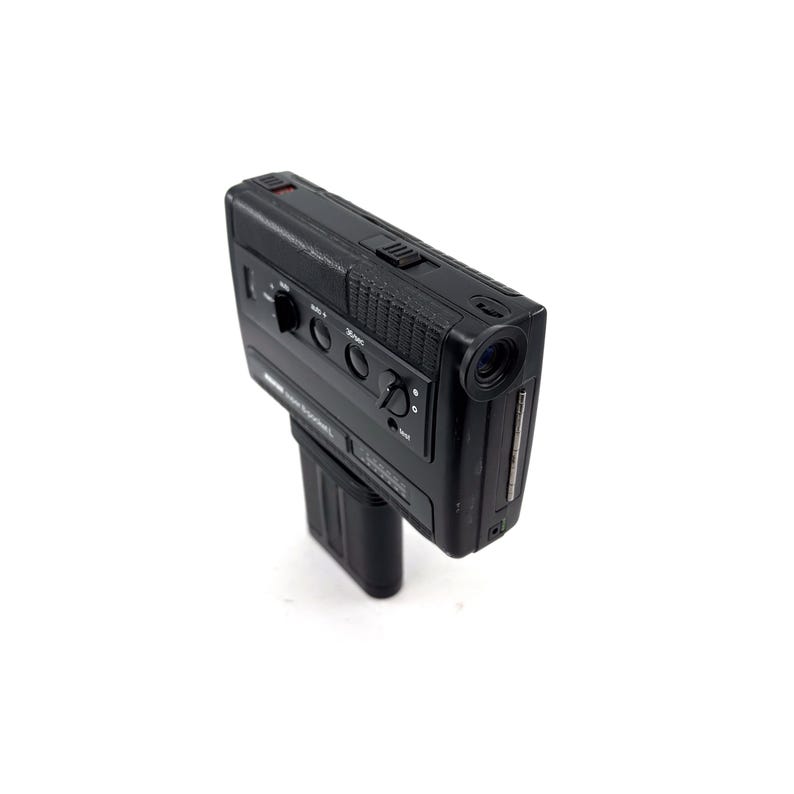 May include: A black vintage video camera with a lens on the front and a series of buttons and dials on the top.
