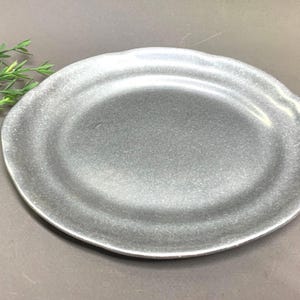 Puede incluir: Un plato ovalado de color plateado con una superficie texturizada. El plato tiene un borde ligeramente ondulado y un brillo metálico. El plato es adecuado para servir alimentos.