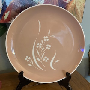 Pode incluir: Um prato de jantar de cerâmica rosa com um design floral branco. O prato tem uma borda ligeiramente elevada e um acabamento liso e brilhante.