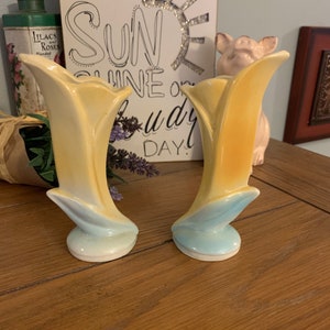 Puede incluir: Un par de jarrones de cerámica amarillos y azules con forma de tulipán. Los jarrones están sobre una superficie de madera.