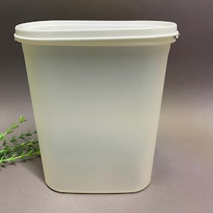 May include: A tall, rectangular, off-white plastic container with a matching lid. The container has a slightly translucent appearance and a smooth surface. The lid fits snugly on top, creating a tight seal. The container is designed for storage.