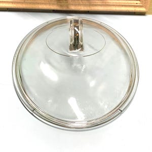 Puede incluir: Tapa de vidrio transparente con asa de plástico. La tapa tiene un borde elevado alrededor del borde.