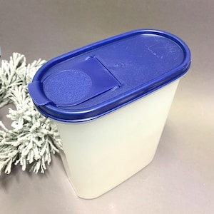 Puede incluir: Un recipiente rectangular blanco para guardar alimentos con tapa azul. La tapa tiene una abertura abatible y forma ovalada redondeada. El recipiente es de material translúcido y la tapa es de color azul liso. Diseñado para uso en la cocina.