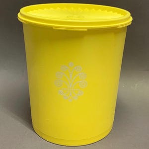 May include: A bright yellow cylindrical plastic storage container with a matching snap-on lid. The front of the container features a white printed graphic consisting of symmetrical swirling lines and small circular accents in a floral-like pattern.