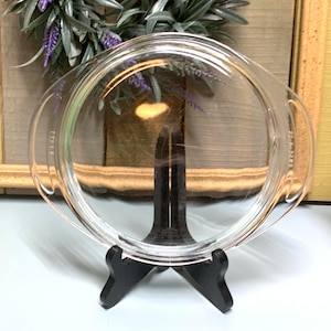 May include: Clear glass pie plate with two handles. The plate is on a black stand.