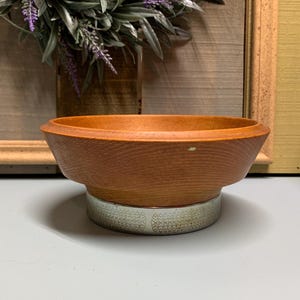 Puede incluir: Un cuenco de madera con una base de plata. El cuenco es marrón y tiene una superficie ligeramente texturizada. La base tiene un patrón decorativo.