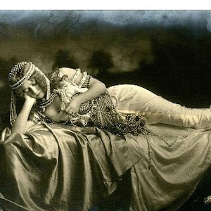 May include: A vintage black and white photograph of a woman wearing a beaded headpiece and a long gown, lying on a bed with a string of pearls draped over her. The image is titled "Strangled with Pearls" and is labeled "Boudoir Fragrance" with the text "CURIO CAULDRON".