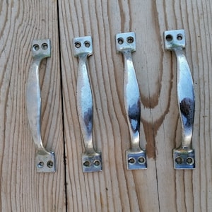 Könnte beinhalten: Vier silberne Türklinken mit polierter Oberfläche. Die Griffe haben ein schlichtes, rechteckiges Design mit abgerundeten Kanten.