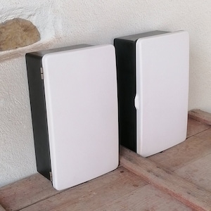 May include: Two white and black electrical boxes with hinged doors. The boxes are made of plastic and have a simple design.